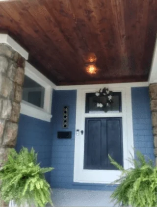 The porch after: blue siding, white trim, black front door with a wreath, and a rich stained wood ceiling