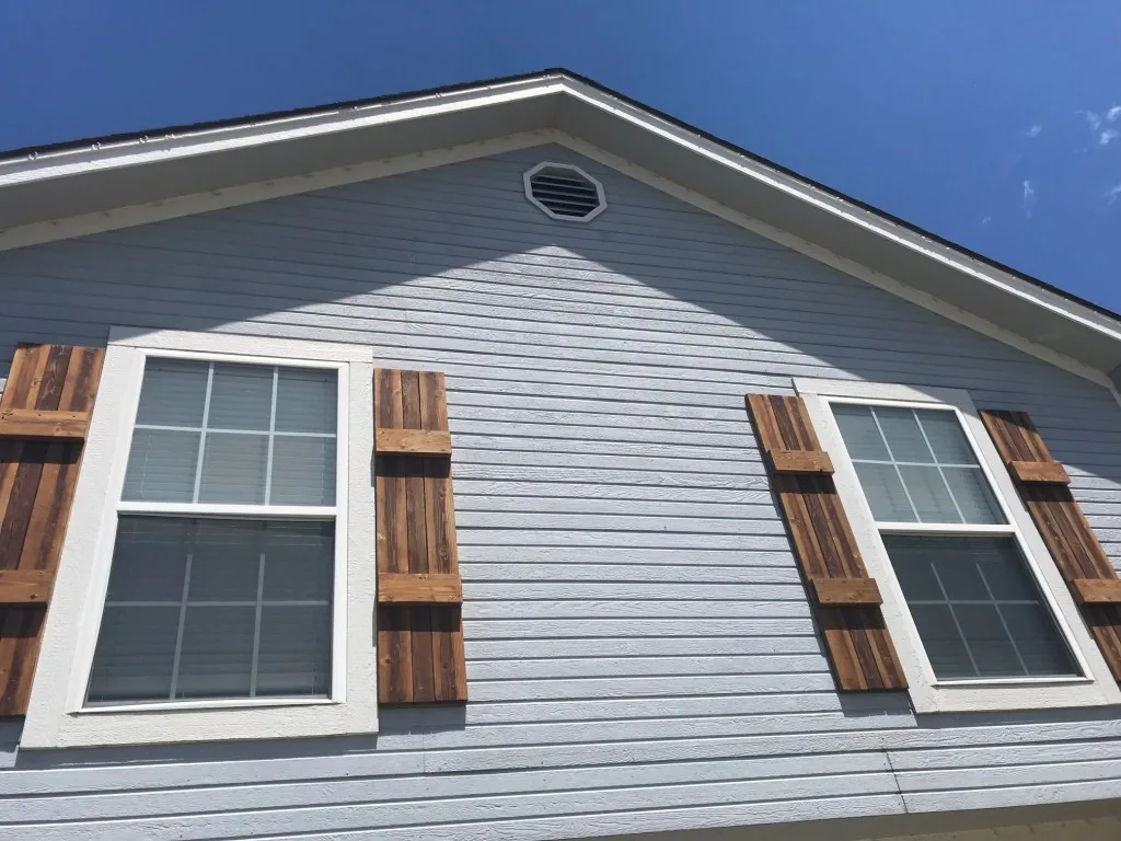 Freshly painted gray siding and white trim under a blue sky, with custom cedar board shutters on both windows